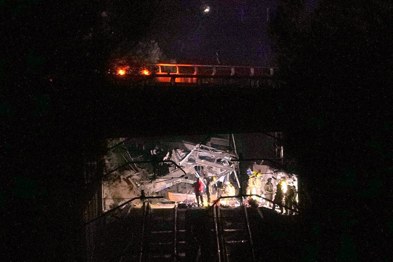 night scene of rubble of collapsed wall illuminated by search and rescue lighting with train visible above